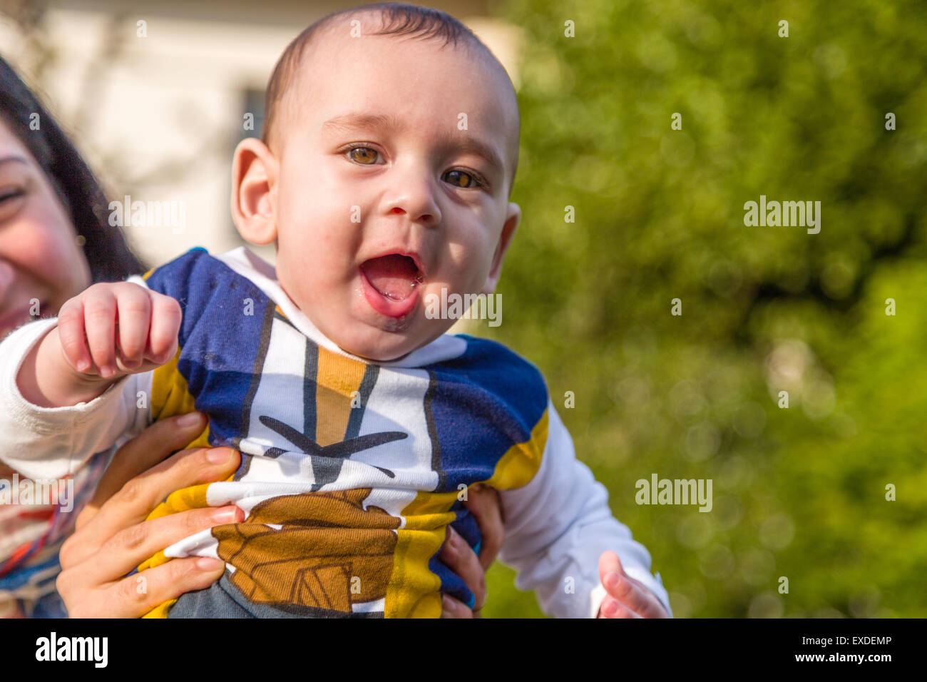 Carino 6 mesi baby con luce marrone capelli in bianco, blu e bruno camicia a maniche lunghe è abbracciato e tenuto da sua madre: sembrano molto felice Foto Stock