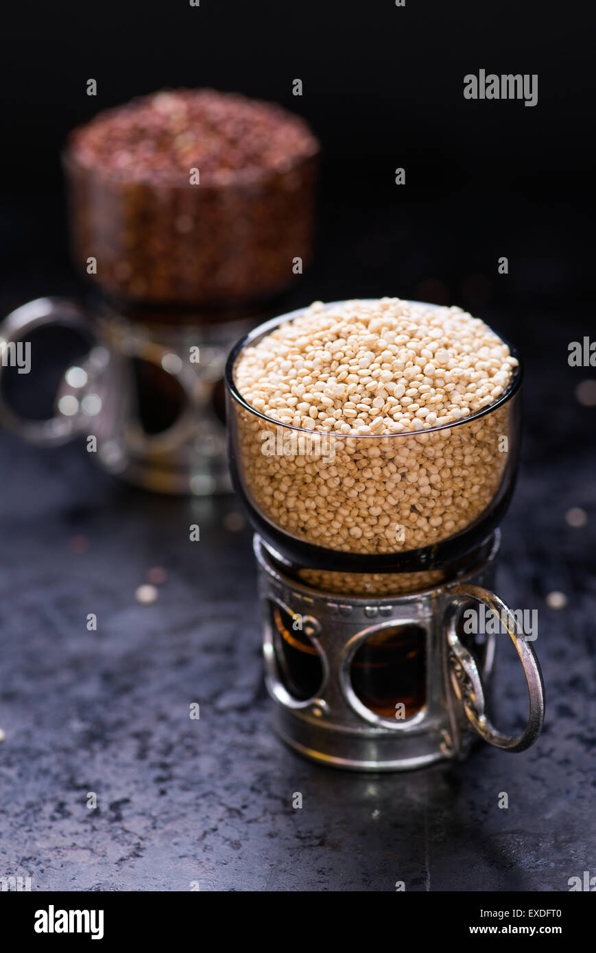 Bianco quinoa raw in un bicchiere di vetro, quinoa rosso sul retro, sfondo scuro, il fuoco selettivo Foto Stock