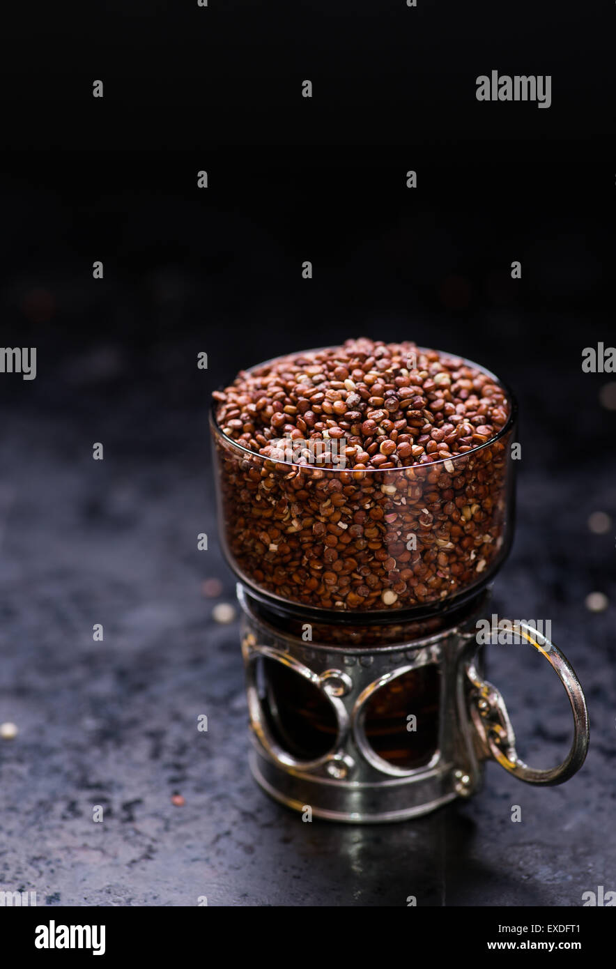 Red raw di quinoa in un bicchiere di vetro, sfondo scuro, il fuoco selettivo Foto Stock