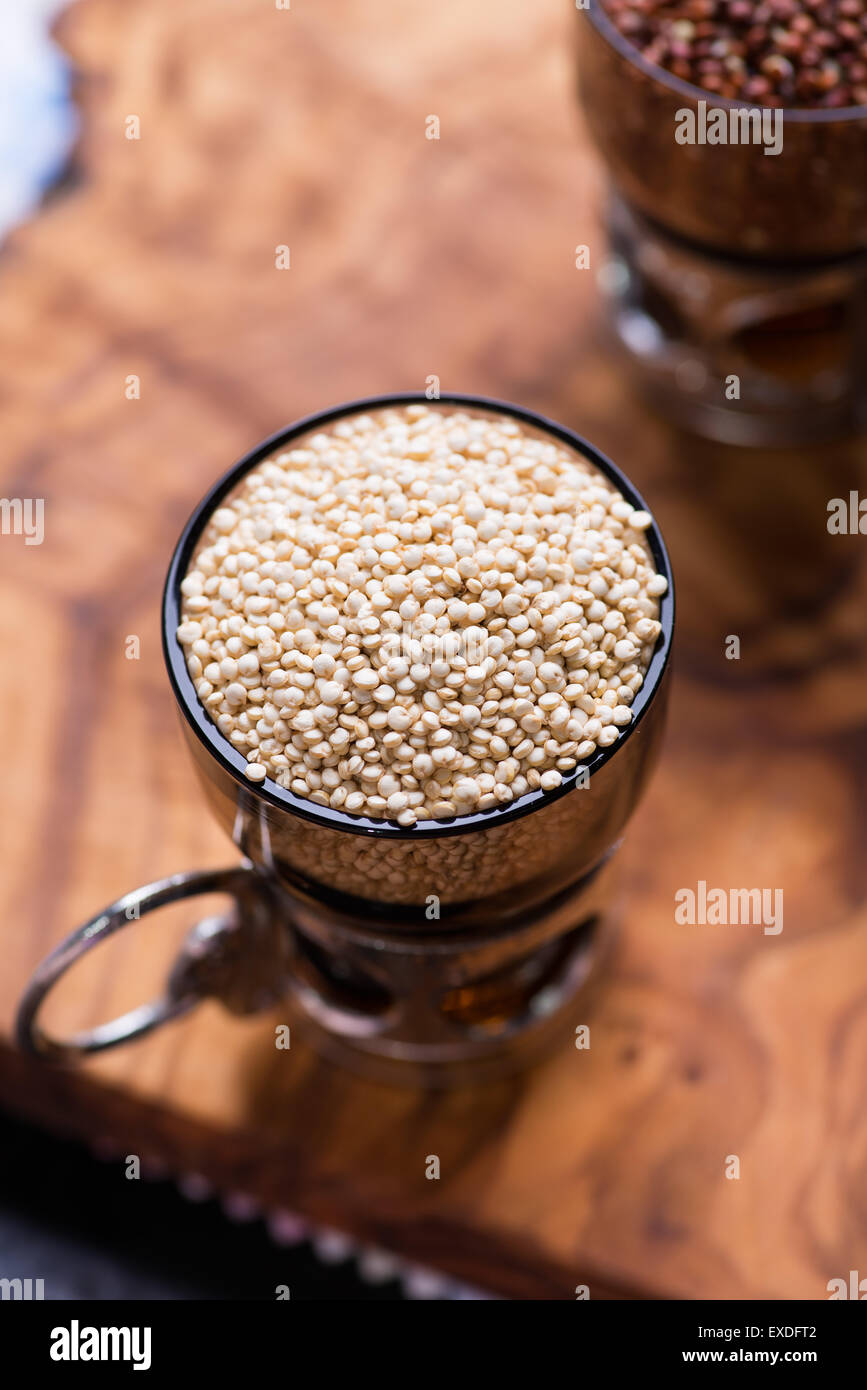 Bianco quinoa raw in un bicchiere di vetro, quinoa rosso sul retro, in legno di olivo di sfondo, il fuoco selettivo, vista dall'alto Foto Stock