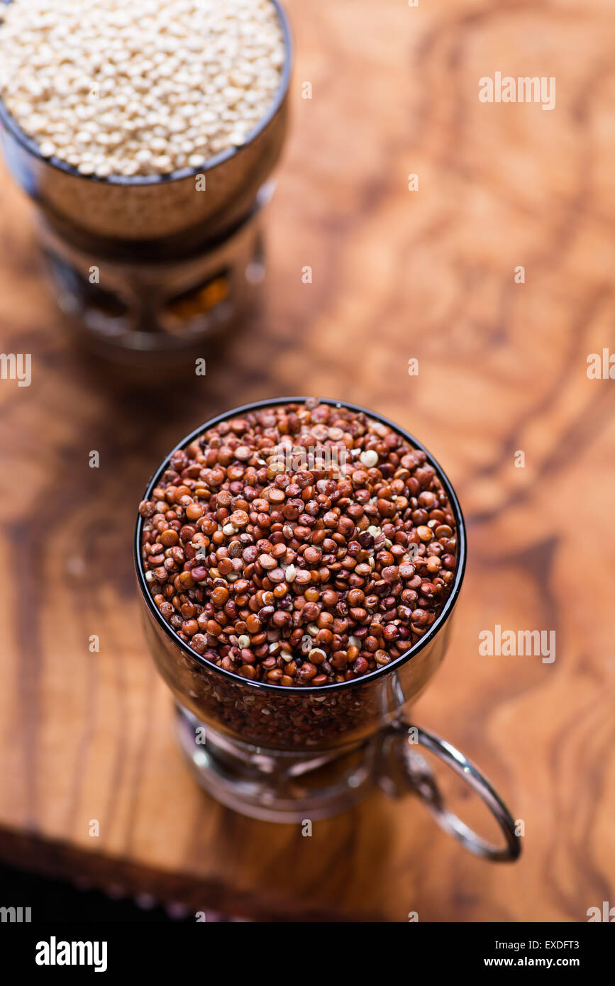 Red raw di quinoa in un bicchiere di vetro, legno d'ulivo sfondo, il fuoco selettivo, vista dall'alto Foto Stock