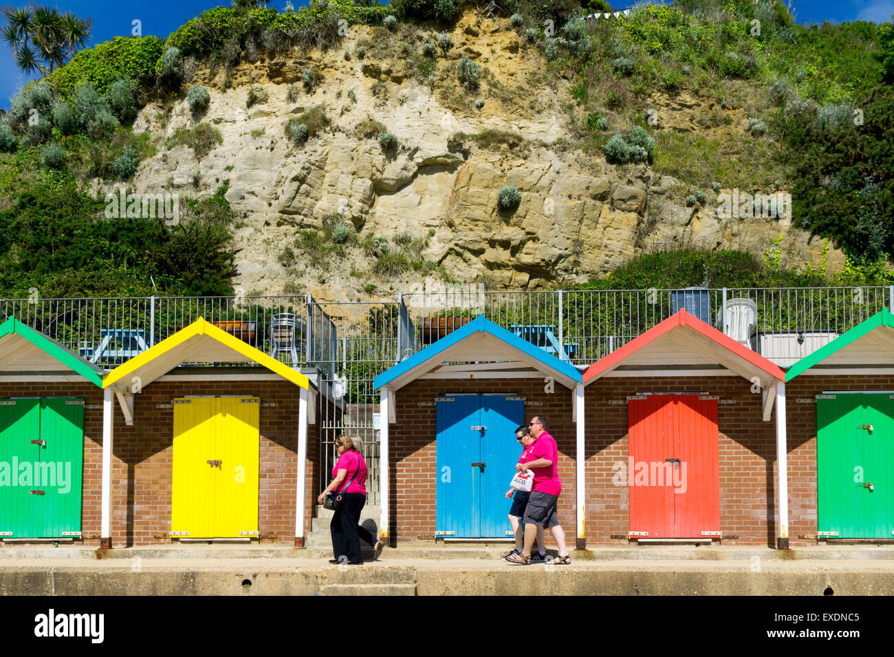 La gente camminare passato dipinto luminosamente beach capanne in Swanage, Dorset, Regno Unito Foto Stock