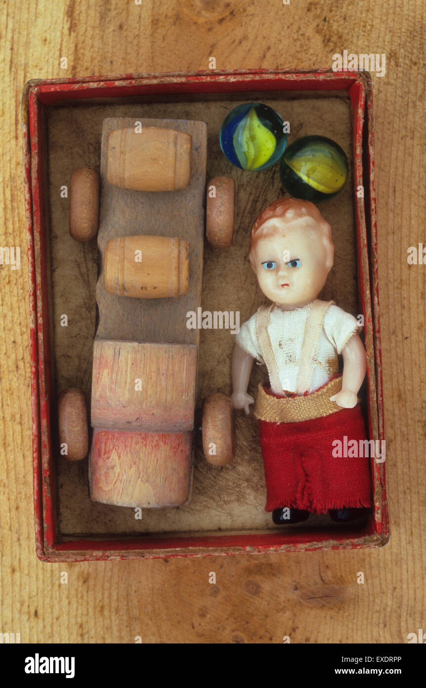 Vintage boy doll giacente nella piccola casella rossa accanto al barile di legno autocarro e biglie di vetro Foto Stock