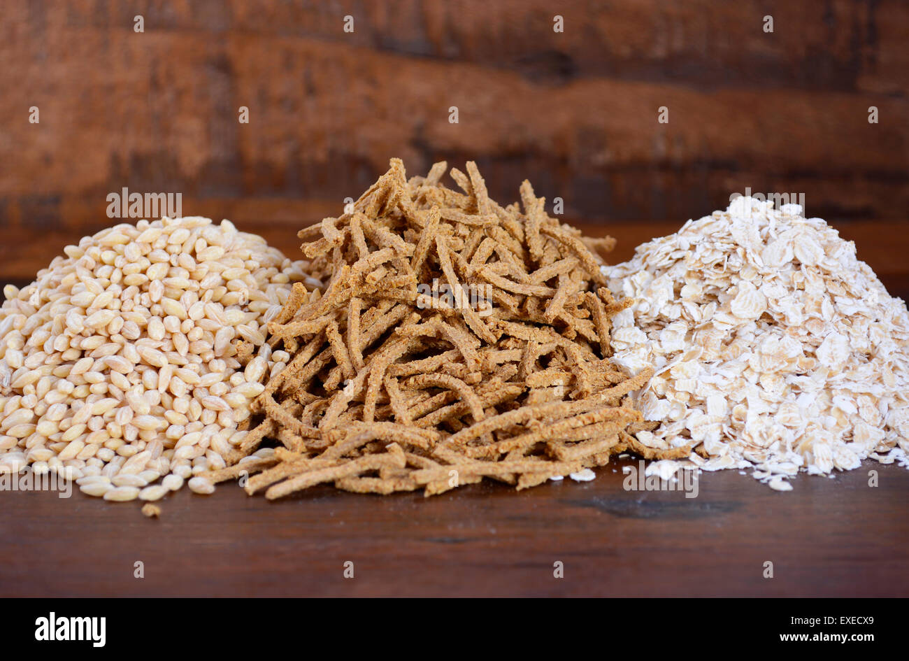Pila di sano ad alto contenuto di fibre prebiotiche comprendente grani di crusca di frumento cereali, fiocchi di avena e di orzo perlato, su rustiche in legno scuro tabella Foto Stock