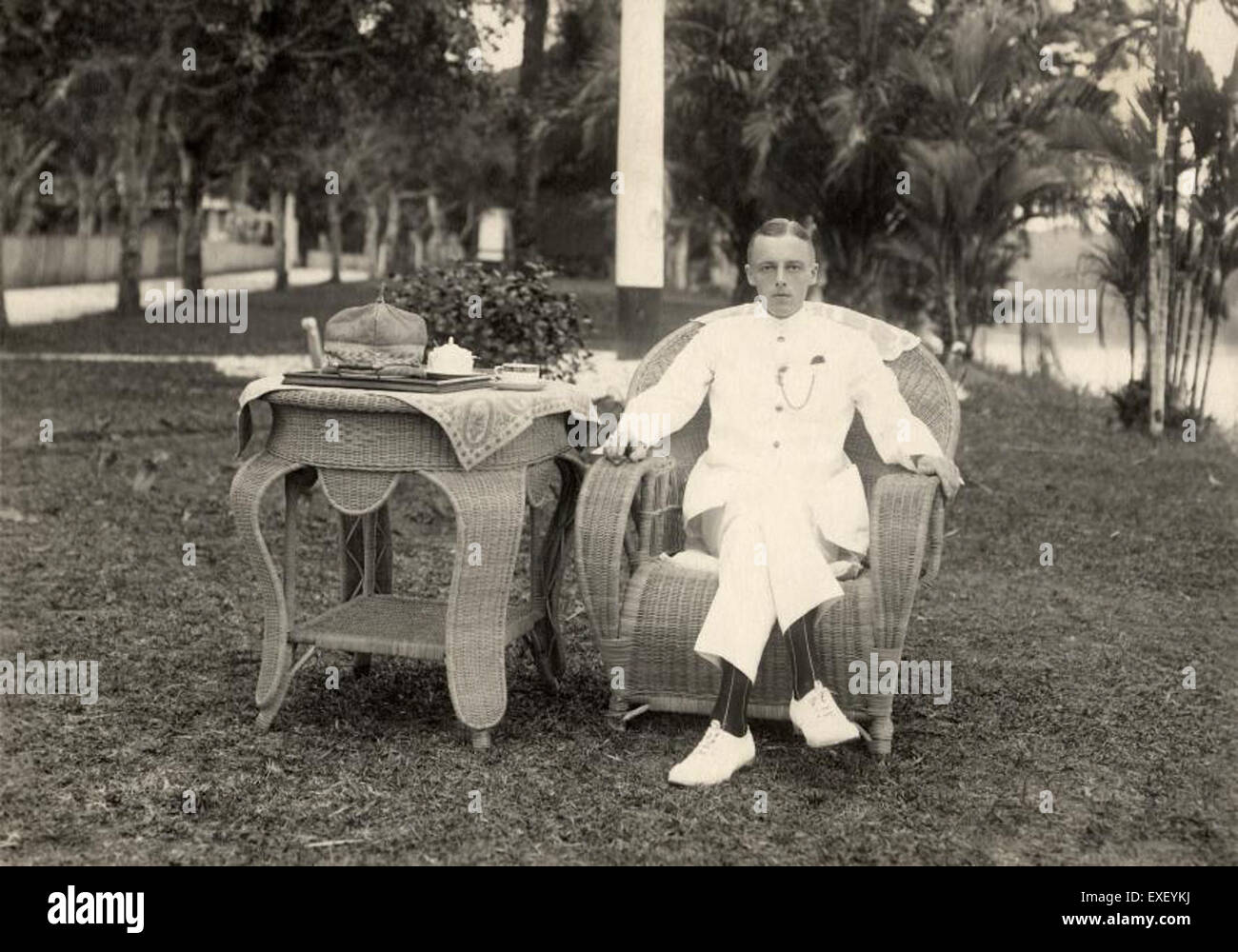 Un uomo olandese in abito tropicale siede su una sedia di vimini, riflettendo una scena del periodo coloniale. Questa immagine cattura la moda e lo stile di vita degli europei nelle regioni tropicali durante l'epoca. Foto Stock
