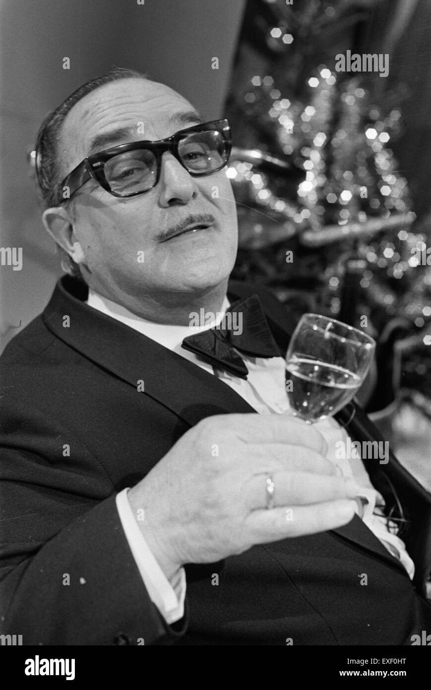 La fotografia del 1974 cattura la produzione di "Sjef van Oekel", una serie televisiva olandese. Lo spettacolo, con il personaggio comico di Sjef, fu popolare durante gli anni '1970 nei Paesi Bassi, specialmente durante la stagione natalizia. L'immagine mostra i momenti dietro le quinte durante le riprese speciali di Natale, riflettendo l'umorismo e il fascino della televisione olandese degli anni '1970. Foto Stock