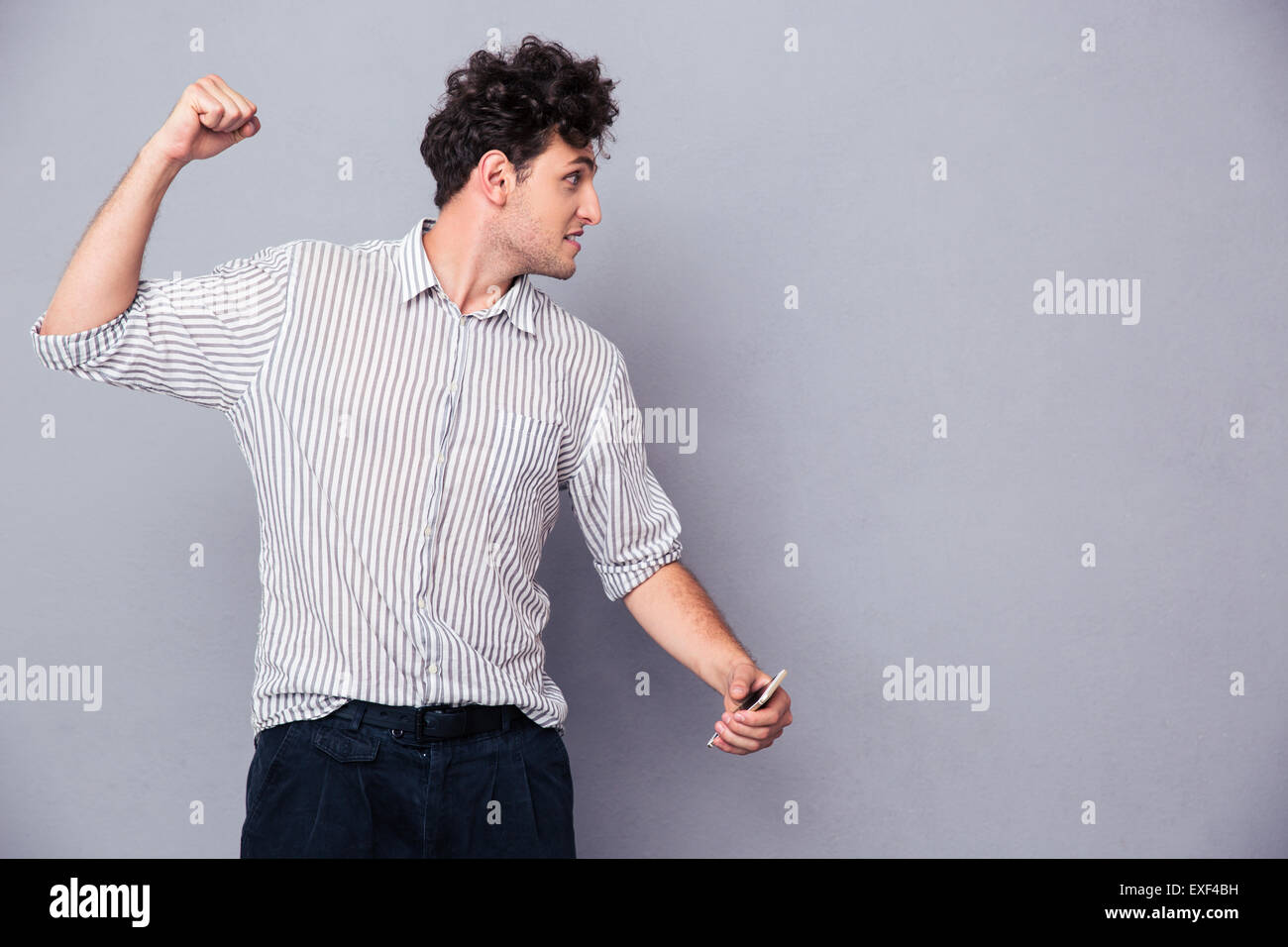 Iracondo con lo smartphone stringendo il pugno su sfondo grigio Foto Stock