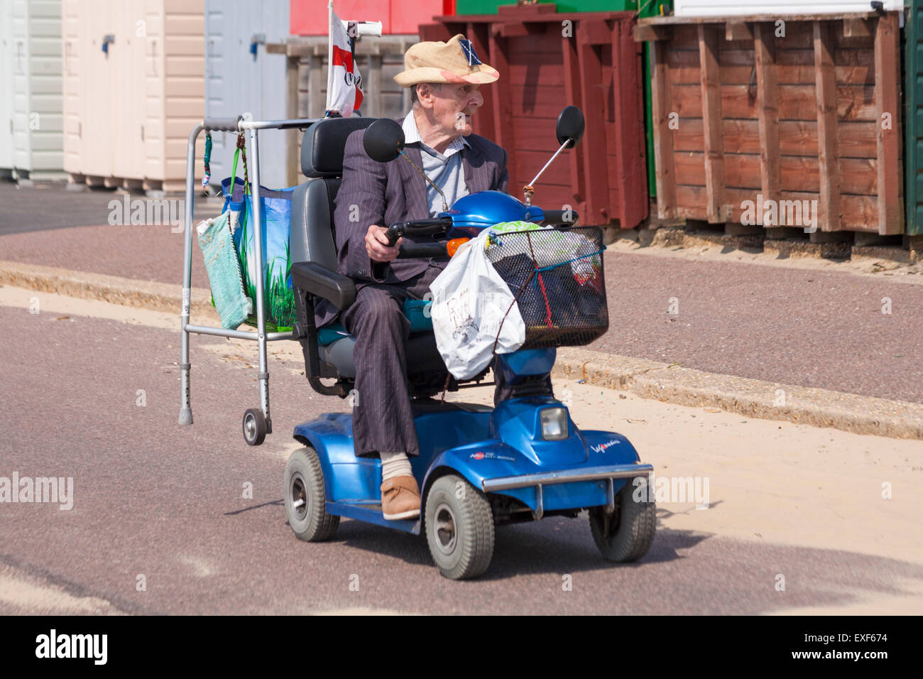 Uomo anziano sulla mobilità scooter passato guida fila di cabine sulla spiaggia, sul lungomare a Bournemouth in luglio Foto Stock