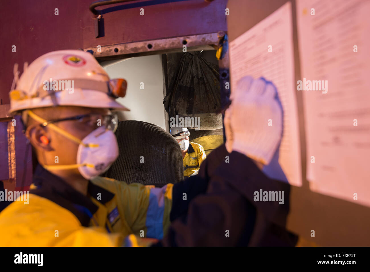 Un tecnico si accoccola all'interno del camino come un collega sta scrivendo sul modulo di checklist dell'attività di manutenzione dell'apparecchiatura alla centrale elettrica di Paiton, Indonesia. Foto Stock
