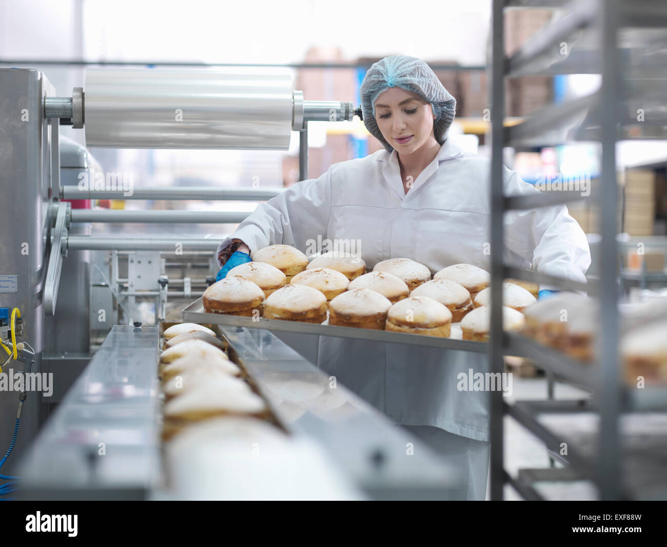 Il panettiere femminile mettendo torte sulla linea di confezionamento in fabbrica di torta Foto Stock
