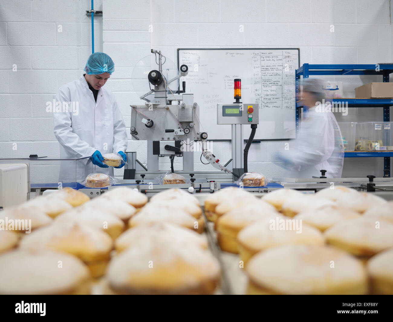 Voce maschile baker mettendo torte sulla linea di confezionamento in fabbrica di torta Foto Stock