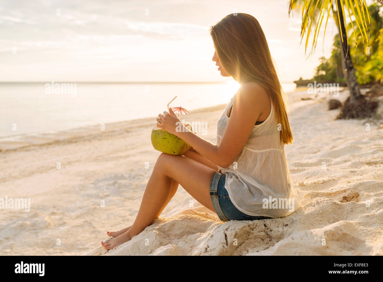 Giovane donna di bere latte di cocco su eun beach, Provincia di Bohol, Filippine Foto Stock