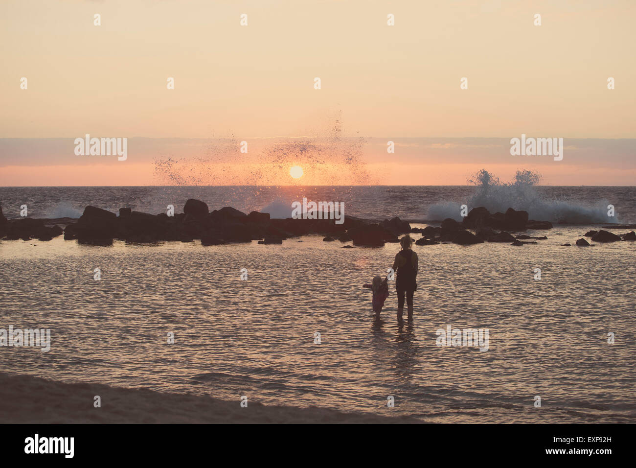 Stagliano madre e bambino femmina paddling in mare guardando a spruzzi delle onde, Kona, Hawaii, STATI UNITI D'AMERICA Foto Stock