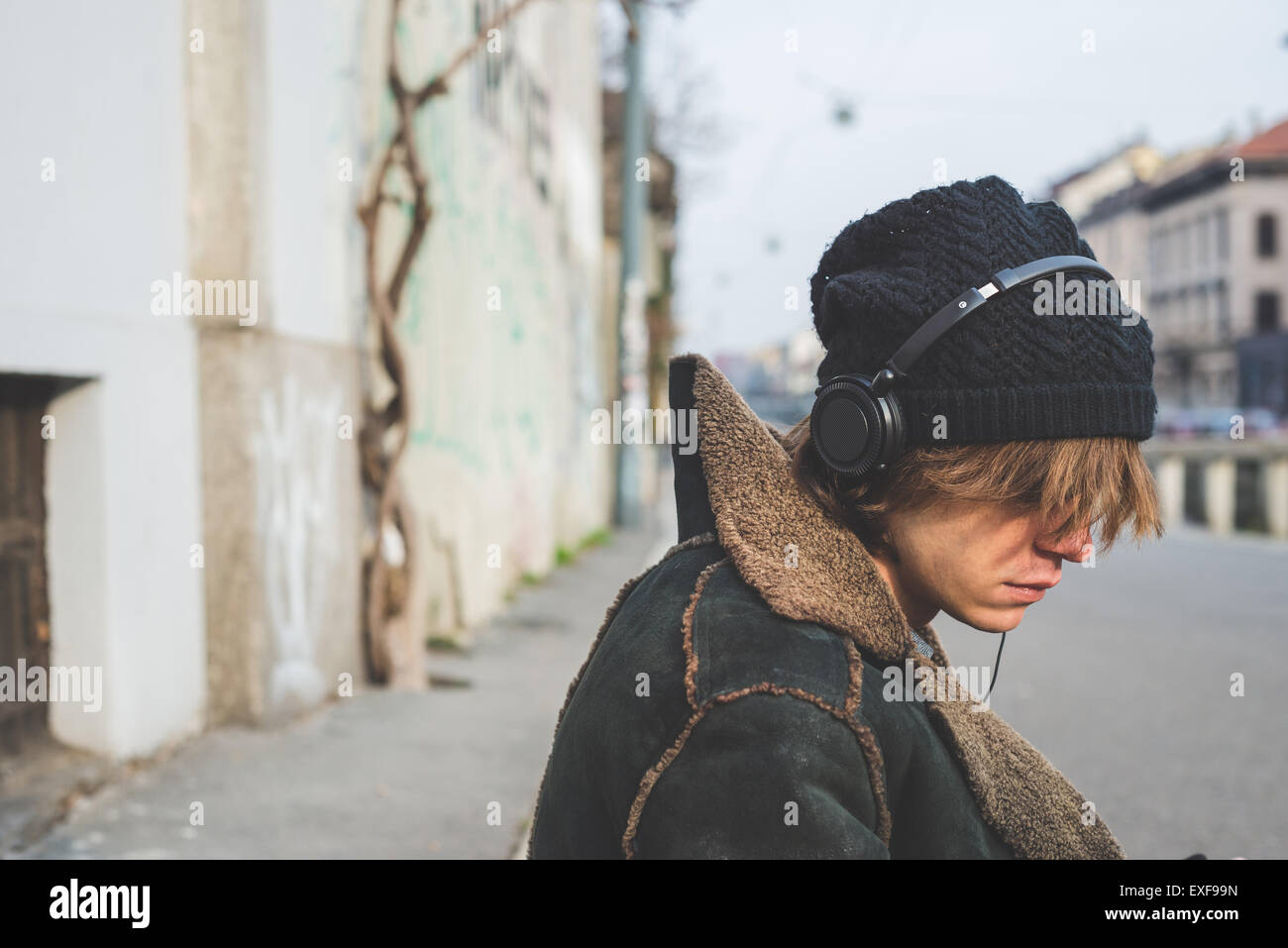 Uomo che ascolta la musica attraverso le cuffie sul cordolo, Milano, Italia Foto Stock