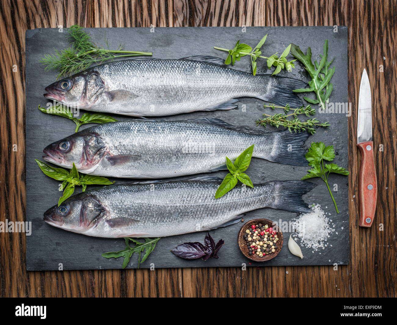 Tre pesci - spigola su una scheda di grafite con erbe e spezie. Foto Stock