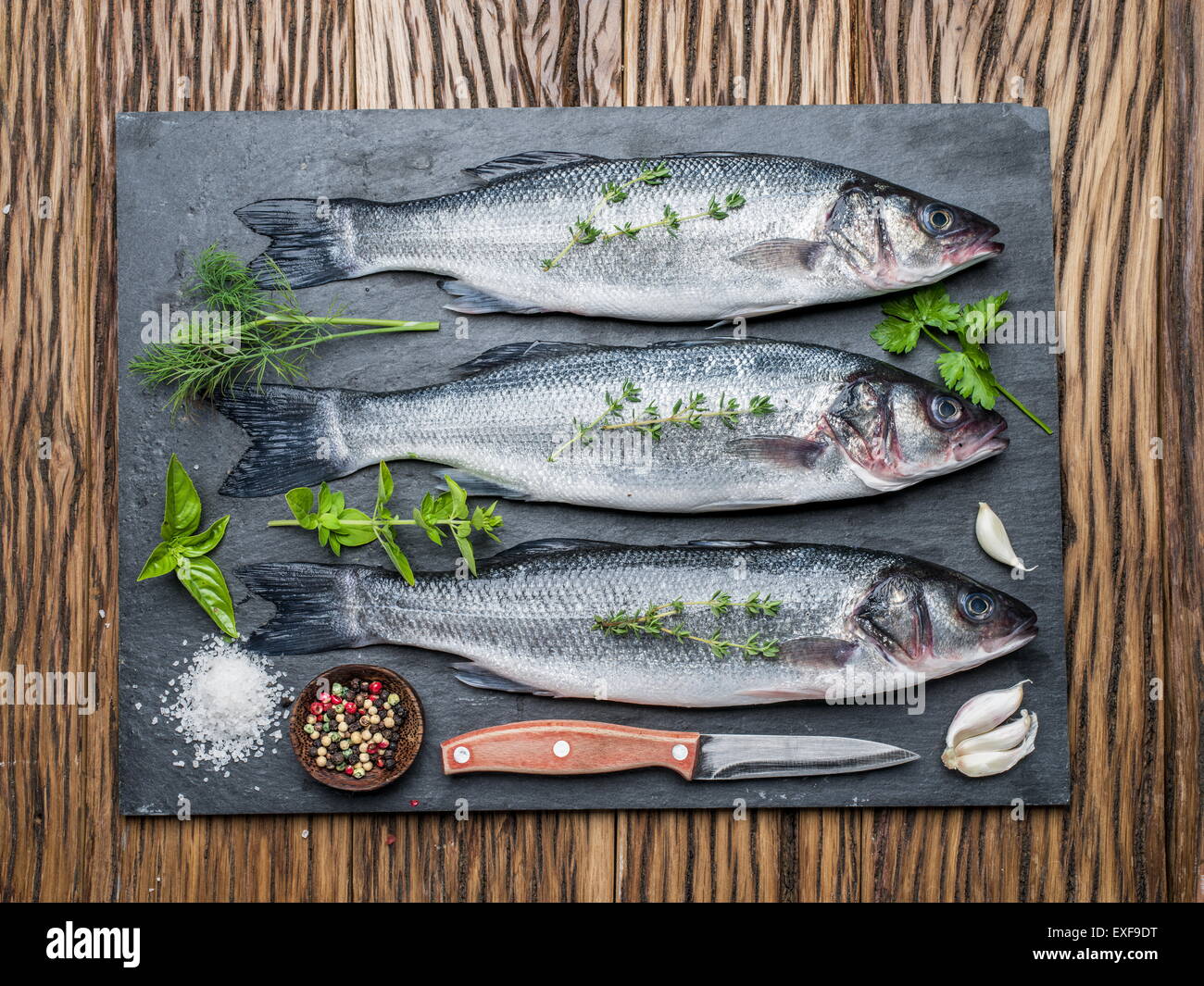 Tre pesci - sea bass su una scheda di grafite con erbe e spezie. Foto Stock