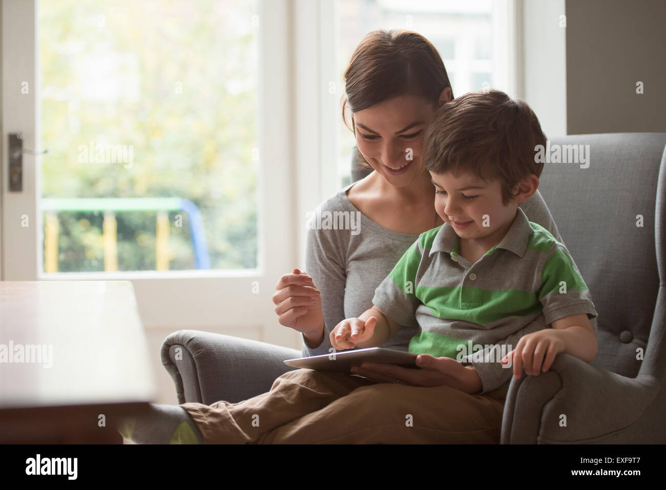 Ragazzo seduto sulla madre di giro e con tavoletta digitale Foto Stock
