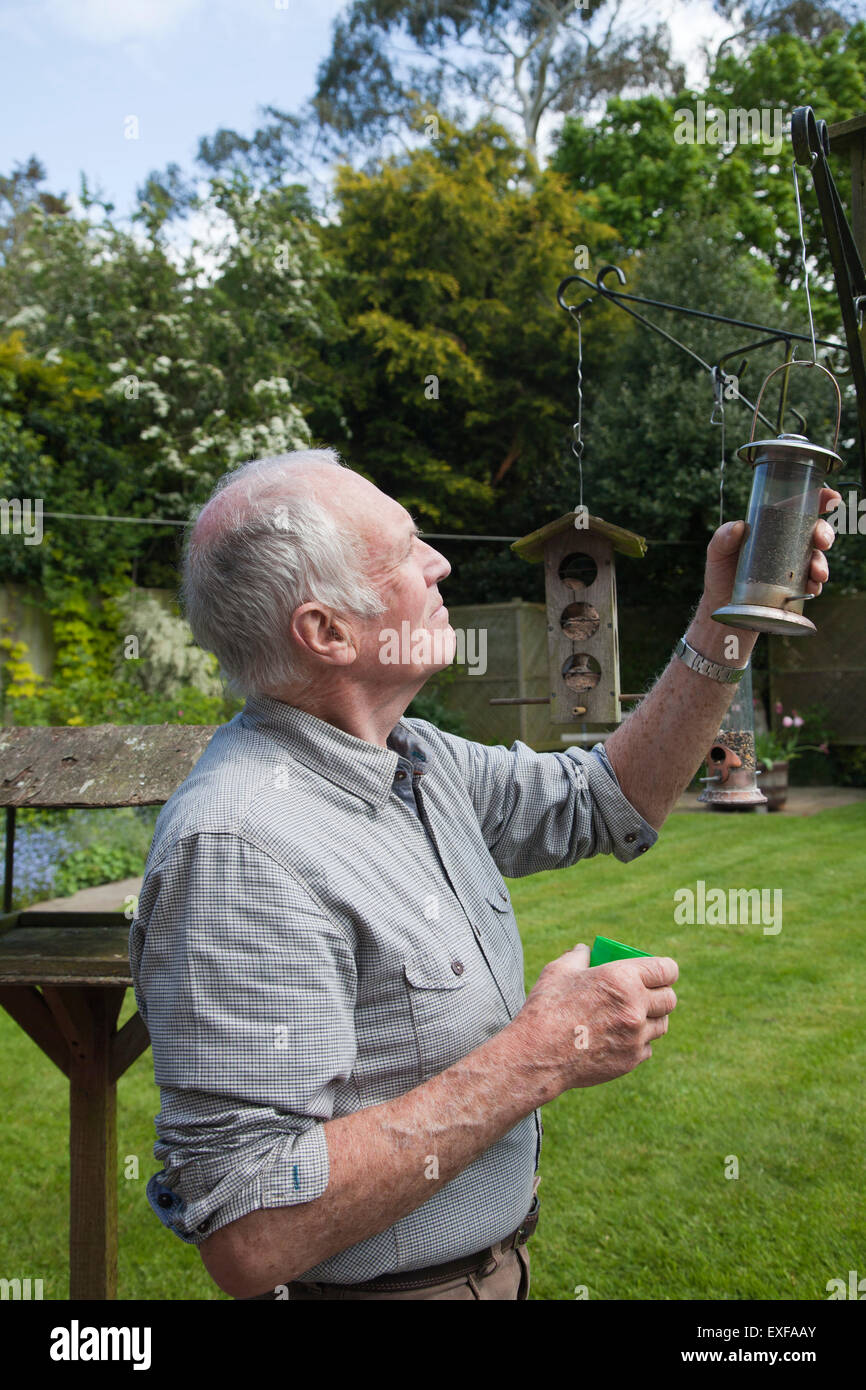 Senior uomo riempimento bird feeder in giardino Foto Stock