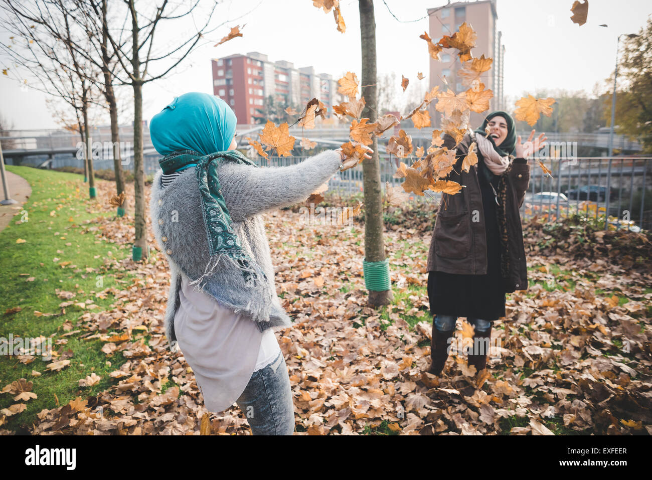 Due giovani donne svolgono combattimenti con foglie di autunno nel parco Foto Stock