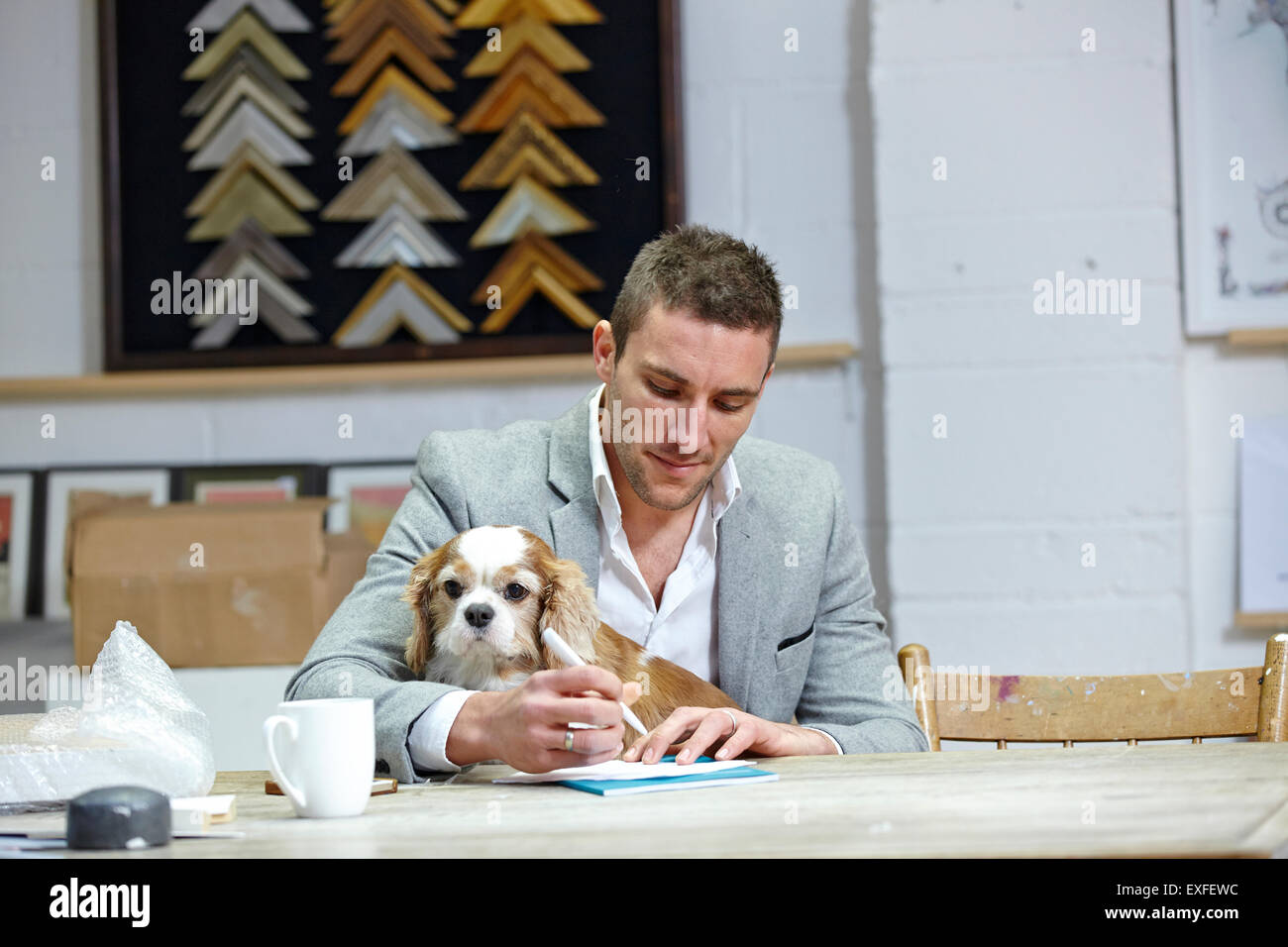 Metà uomo adulto con il cane a rendere note alla scrivania in picture corniciai workshop Foto Stock