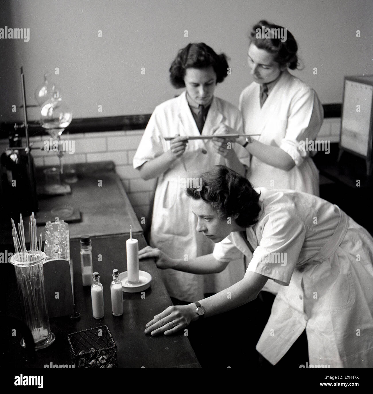 Storico degli anni cinquanta, la femmina di tre studenti di chimica in camici fare esperimenti in laboratorio. Foto Stock