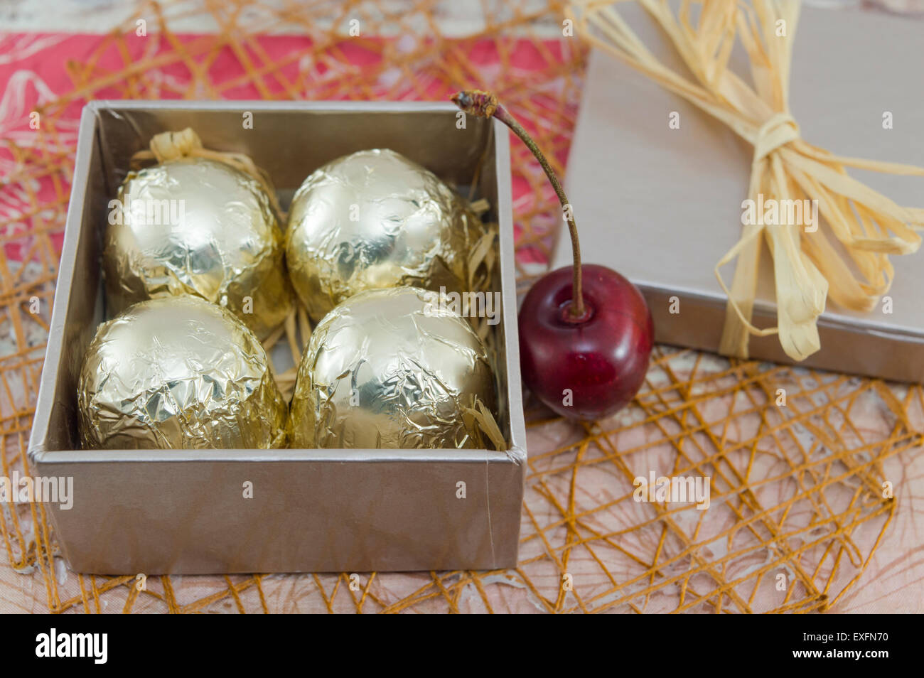 Cioccolatini avvolti in golden confezione colorata in un colore rosso presente scatola con ciliegie fresche Foto Stock