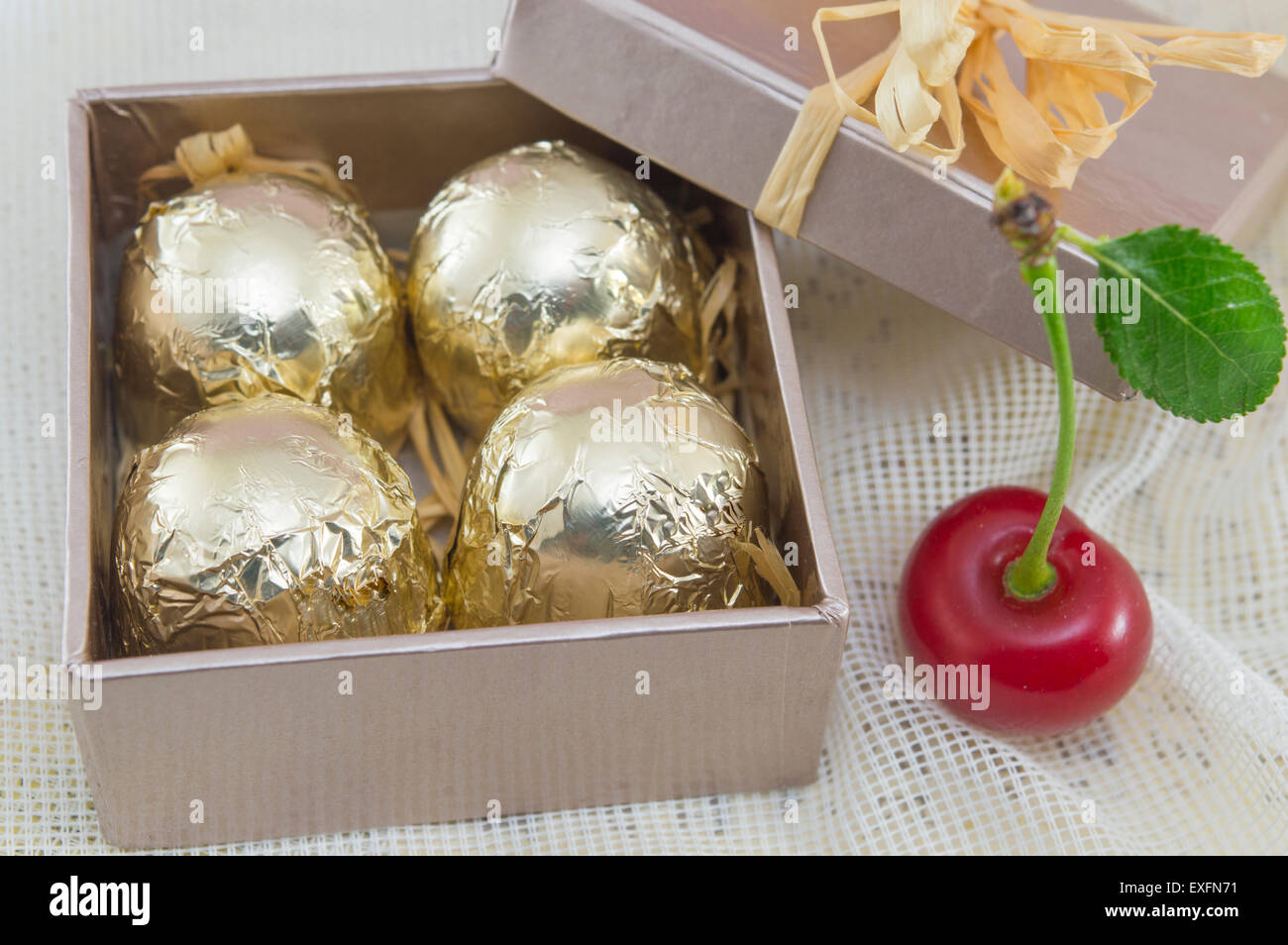 Cioccolatini avvolti in golden confezione colorata in un colore rosso presente scatola con ciliegie fresche Foto Stock