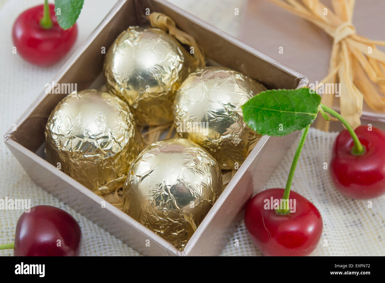Cioccolatini avvolti in golden confezione colorata in un colore rosso presente scatola con ciliegie fresche Foto Stock