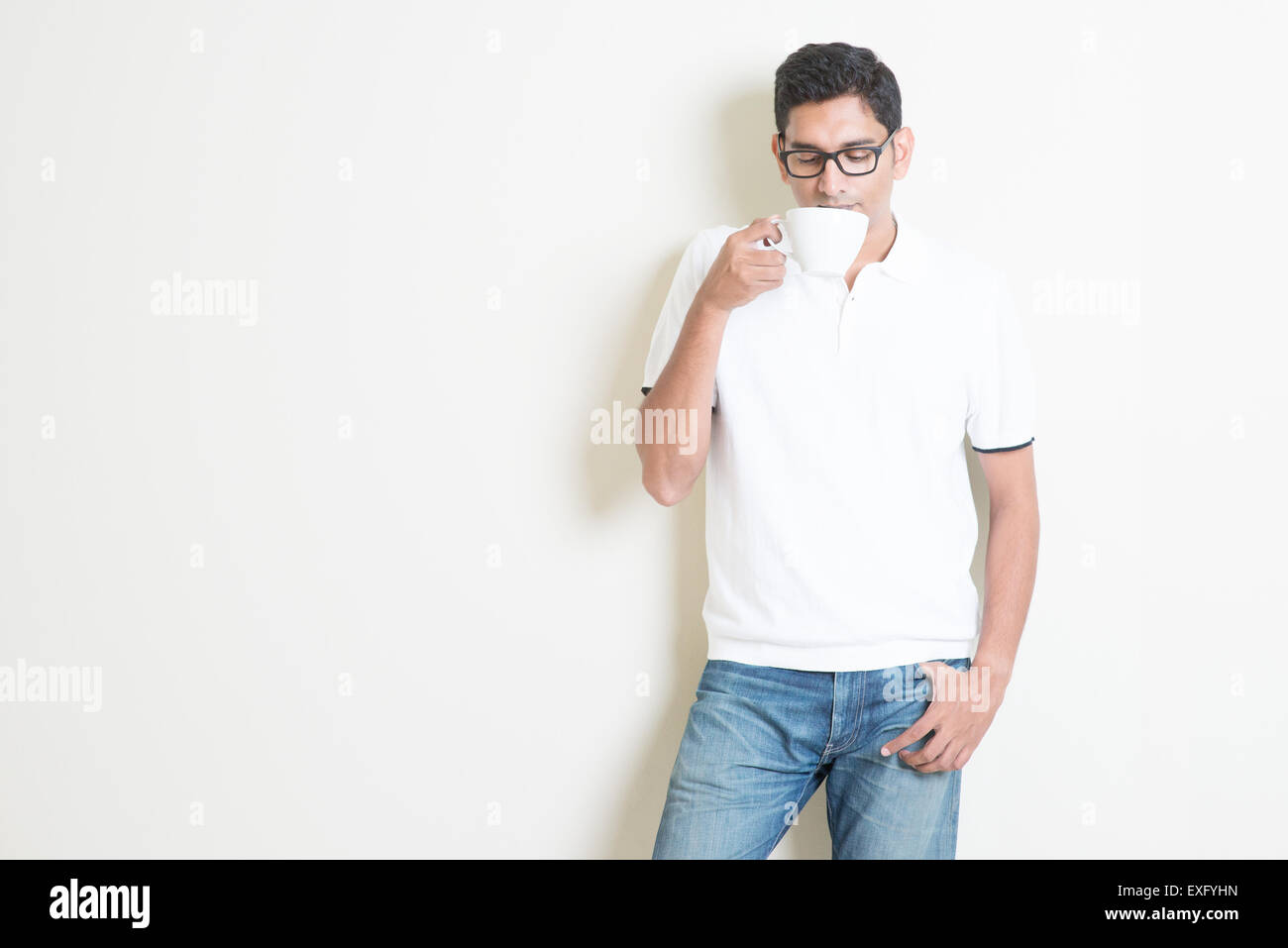 Ragazzo indiano di bere il caffè. Asian permanente sulla pianura sfondo con ombra e copia dello spazio. Bel modello maschile. Foto Stock