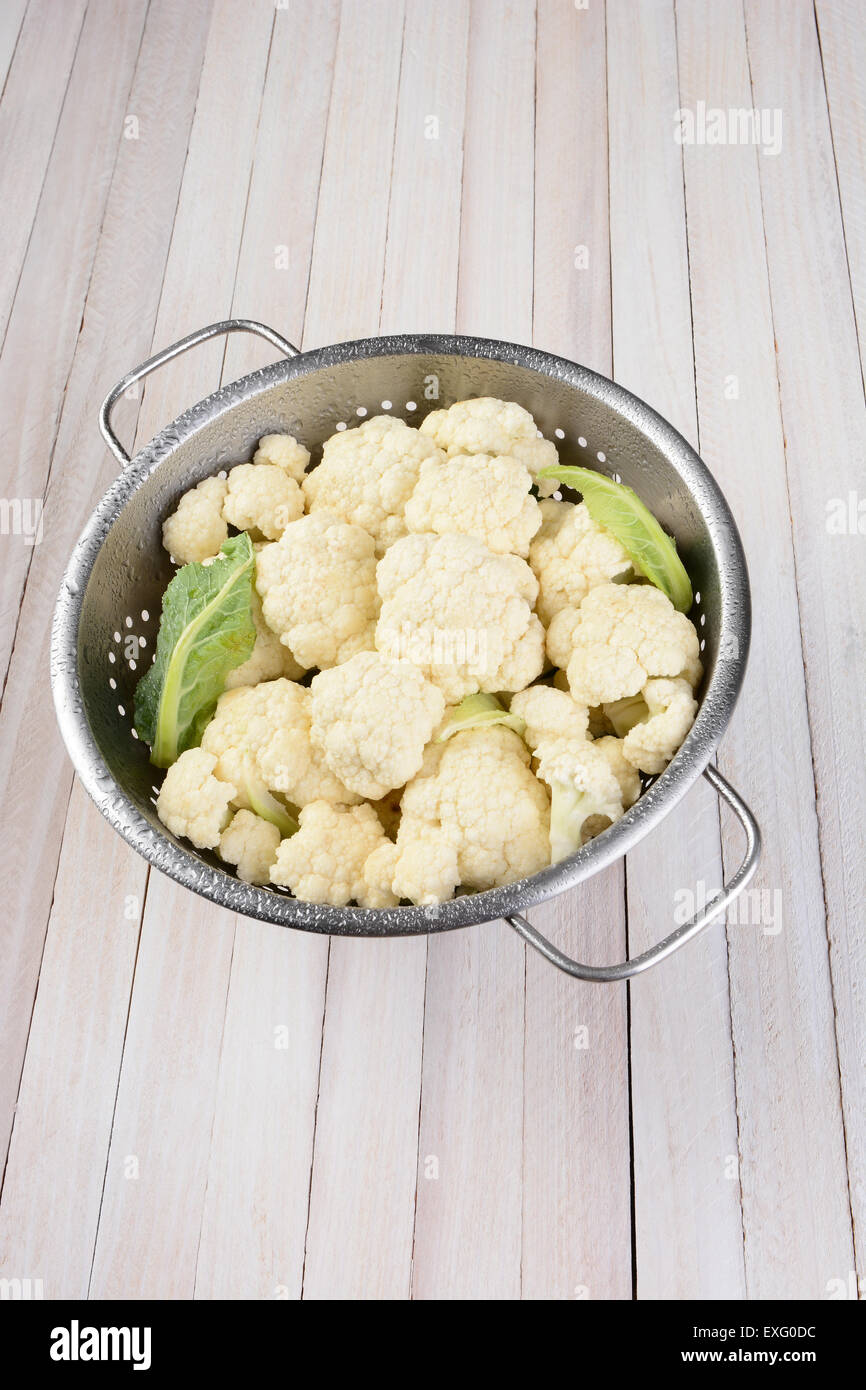 Verticale alto angolo di visione di una testa di cavolfiore in un colapasta di metallo su una tavola in legno rustico, con copia spazio. Foto Stock