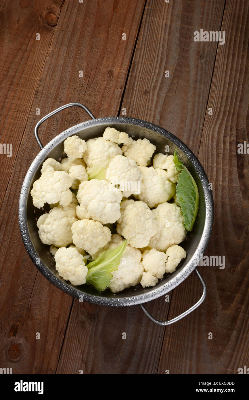 Elevato angolo di visione di uno scolapasta riempito con cime di cavolfiore. Su una tavola in legno rustico. Formato verticale. Foto Stock