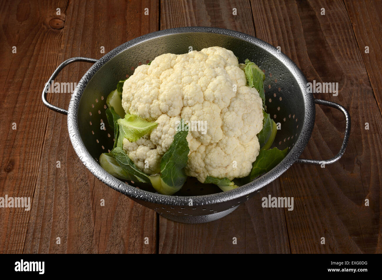 Elevato angolo di visione di uno scolapasta con una testa di cavolfiore. Il filtro è su una tavola in legno rustico e ha bee colmi con acqua Foto Stock
