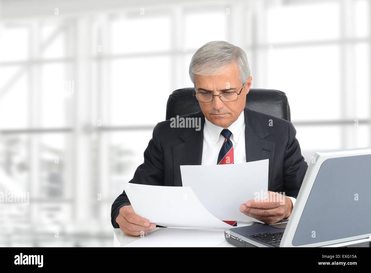 Primo piano di un imprenditore senior guardando i documenti seduto alla sua scrivania in ufficio moderno interno. Formato orizzontale con copia s Foto Stock