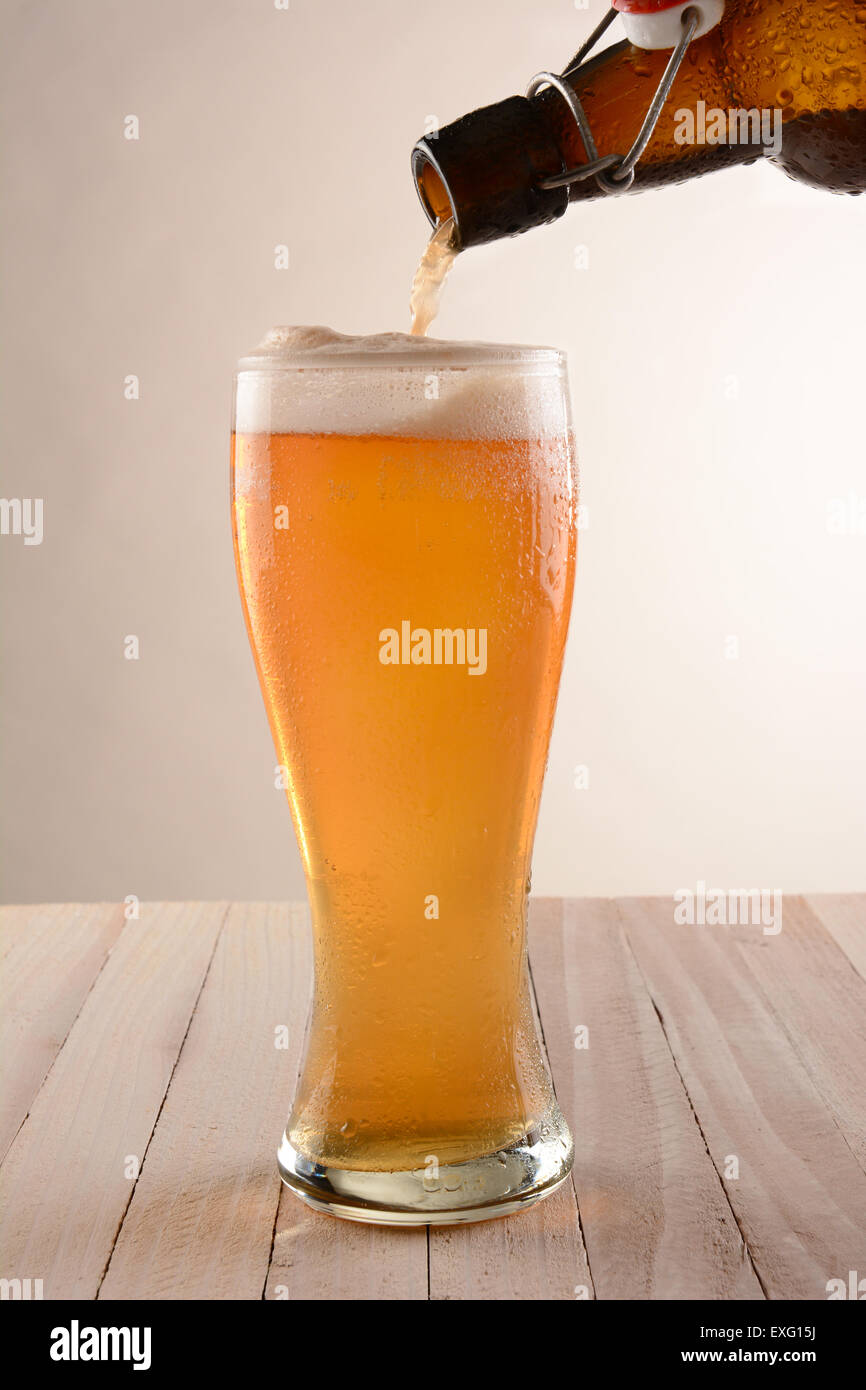 Per spillare la birra in un bicchiere alto da un swing top bottiglia. Su una tavola di legno con una luce ot sfondo scuro. Foto Stock
