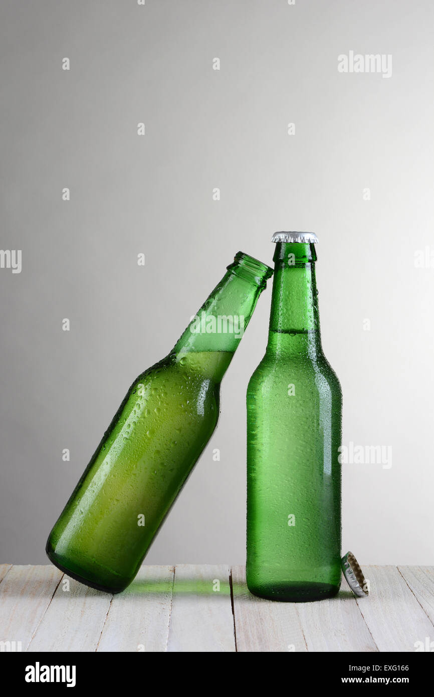 Verde di due bottiglie di birra su una tavola di legno contro una luce di sfondo grigio scuro. Una bottiglia è inclinata appoggiata sull'altro bo Foto Stock