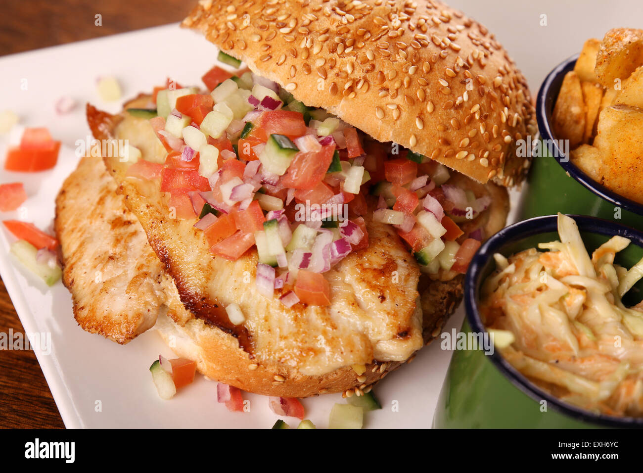 Deliziosi hamburger di pollo tritato con insalata servita con fette di patate su una piastra bianca su di un tavolo di legno. Foto Stock