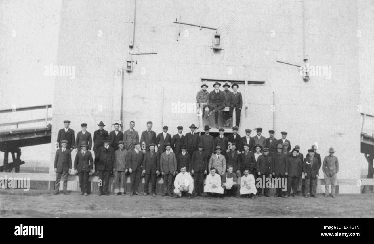 Questa fotografia storica mostra i ragazzi mennoniti che si trovano di fronte a un ascensore per cereali a Fairview, che catturano una scena agricola dei primi anni del XX secolo. L'immagine riflette la vita rurale e l'importanza delle infrastrutture agricole nelle comunità mennonite durante questo periodo. Foto Stock