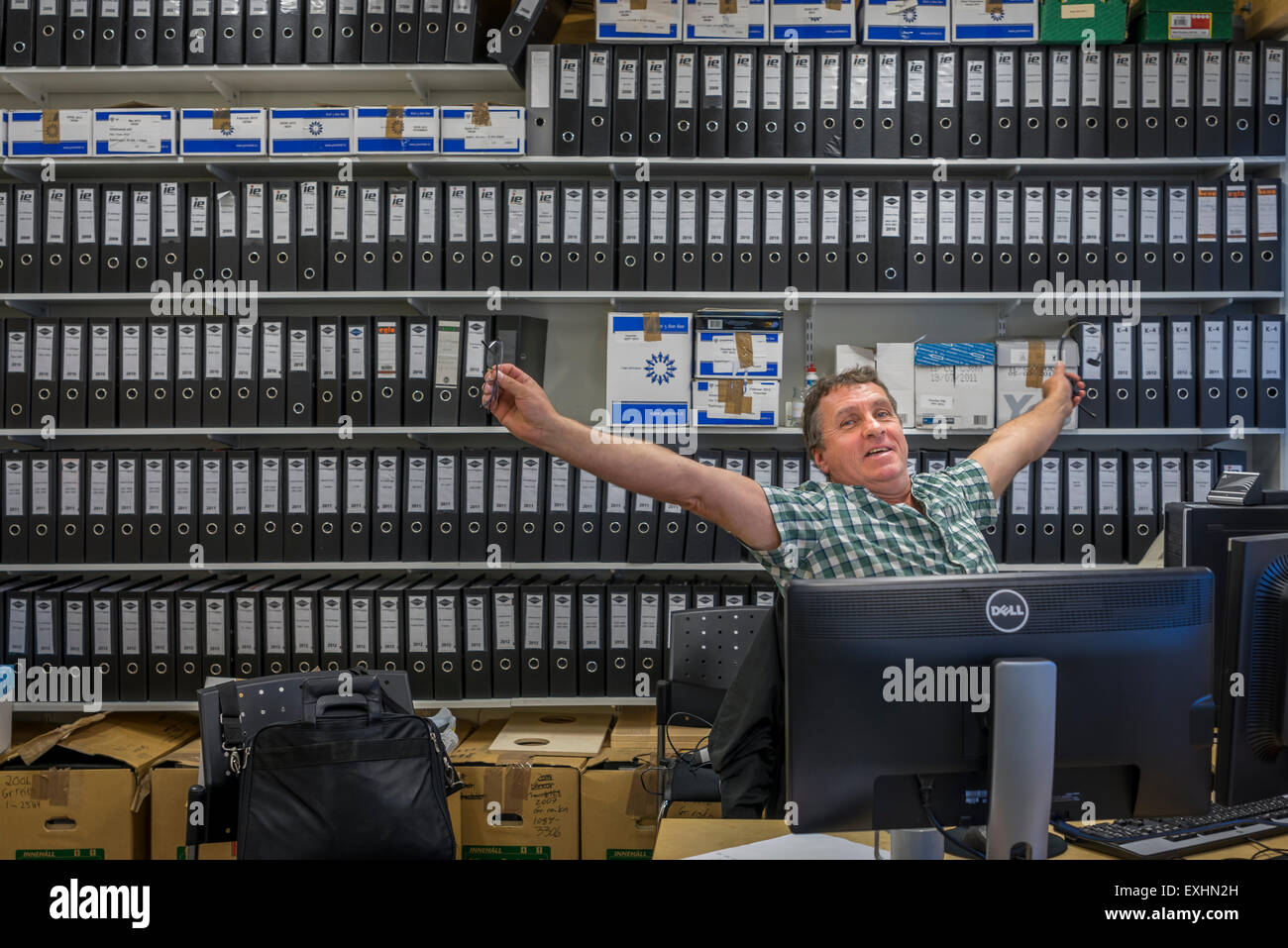 L'uomo stretching mentre è seduto alla sua scrivania in ufficio, Reykjavik, Islanda Foto Stock