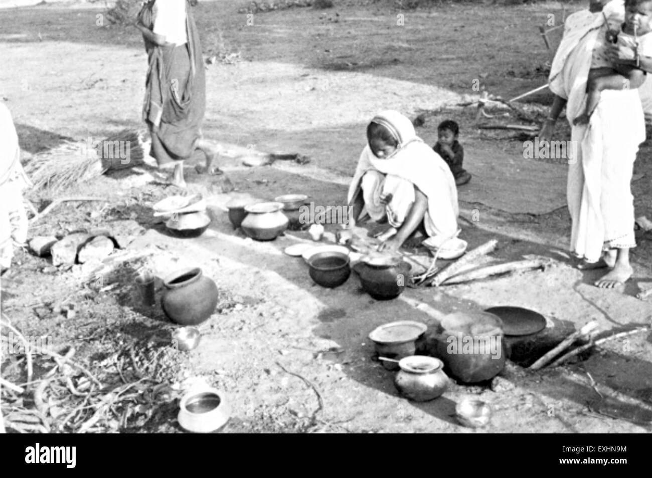 Questa fotografia del 1964 cattura una scena dall'India durante la preparazione di un pasto serale. Riflette le pratiche culinarie tradizionali e la vita quotidiana nelle famiglie indiane durante il tempo. Foto Stock