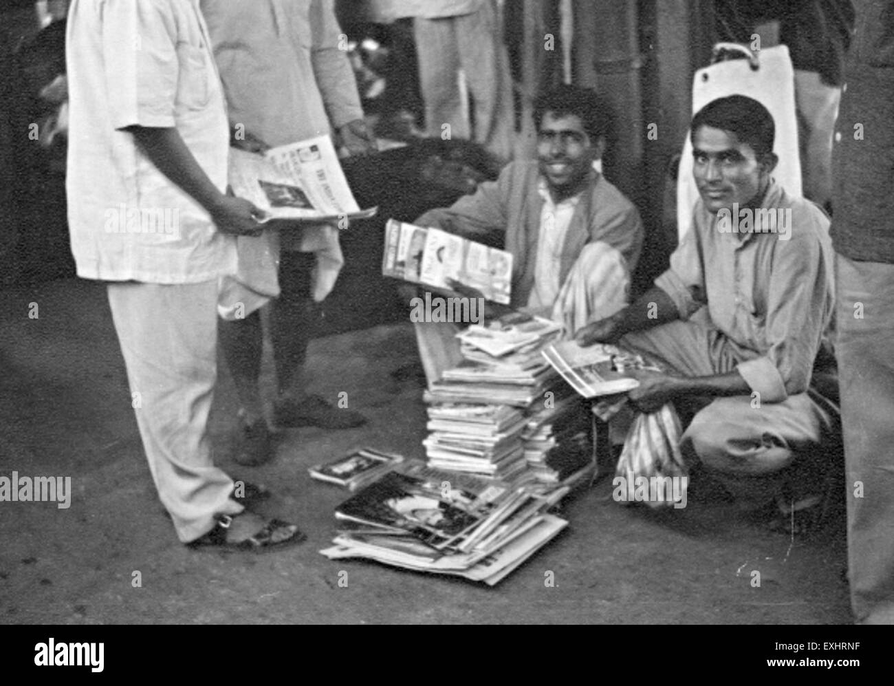 Questa fotografia cattura un venditore di libri in una stazione ferroviaria in India. Si vede che il venditore offre una varietà di libri, tipici dei venditori ambulanti nelle stazioni ferroviarie indiane, dove libri e giornali vengono spesso venduti ai viaggiatori. Foto Stock