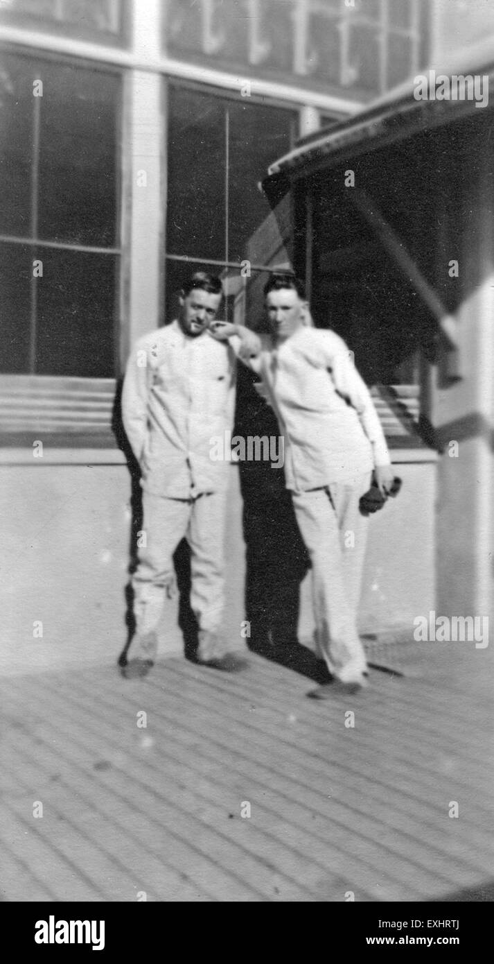 Una fotografia storica con due uomini in piedi davanti a un grande edificio, che catturano un momento nel tempo. La foto enfatizza l'architettura e l'abbigliamento degli individui, offrendo uno sguardo sulla moda e il design degli edifici dell'epoca. Foto Stock