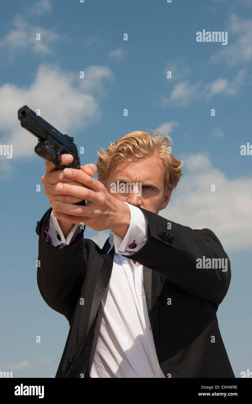 Uomo in possesso di una pistola e mirando a sparare qualcuno , indossando un abito nero. Foto Stock