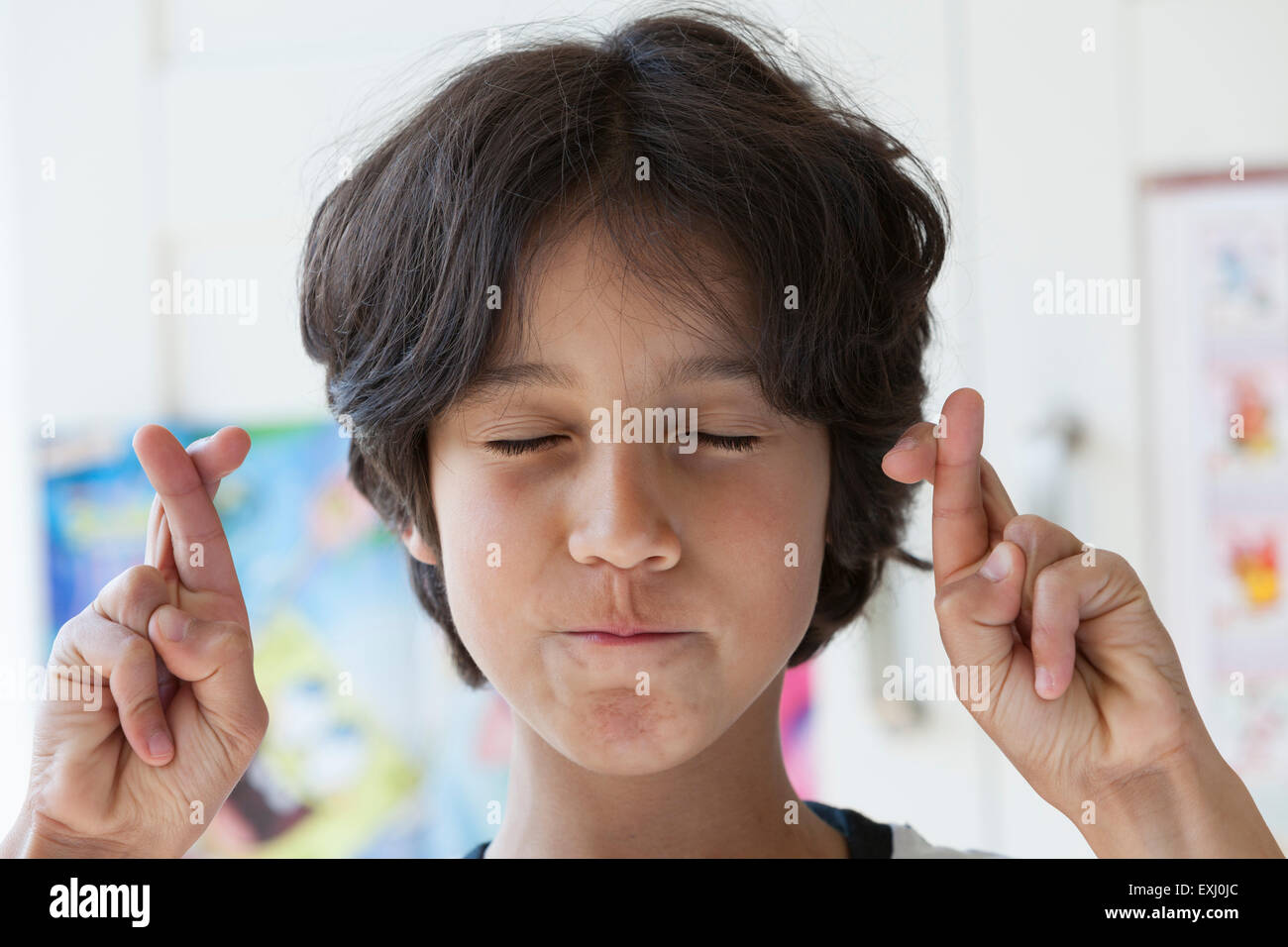 Ragazzo adolescente incrocio le dita con gli occhi chiusi Foto Stock