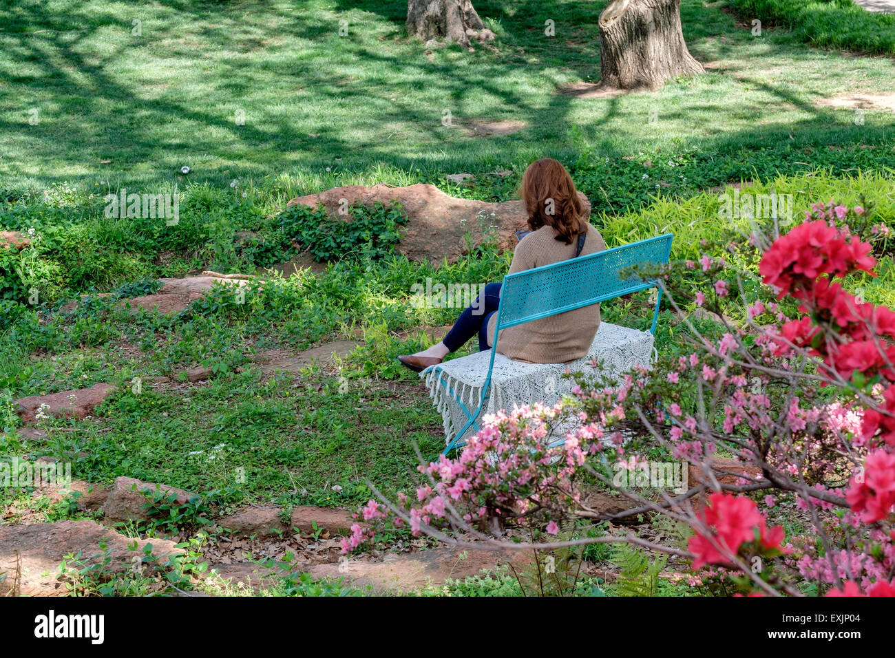 Un caucasico red intitolata donna si siede su una panchina e gode di una giornata di primavera in Will Rogers Park in Oklahoma City, Oklahoma, Stati Uniti d'America. Foto Stock