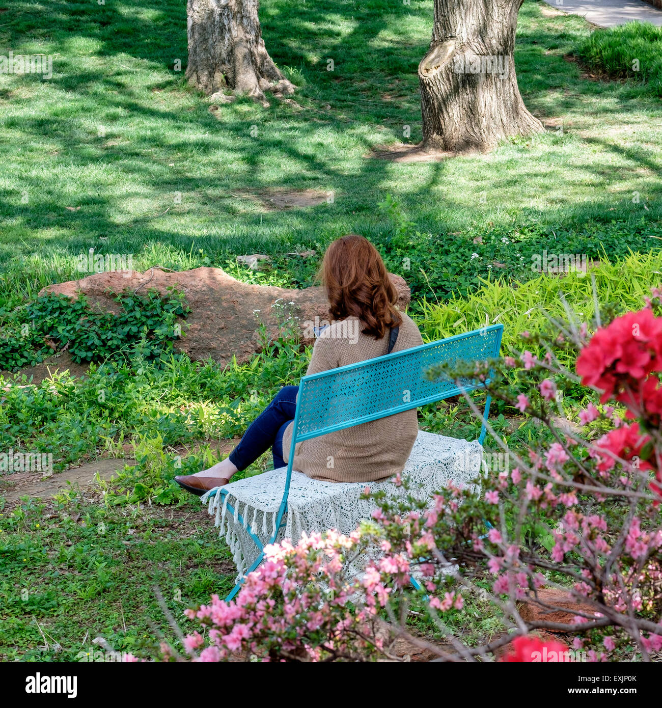 Un caucasico red intitolata donna si siede su una panchina e gode di una giornata di primavera in Will Rogers Park in Oklahoma City, Oklahoma, Stati Uniti d'America. Foto Stock