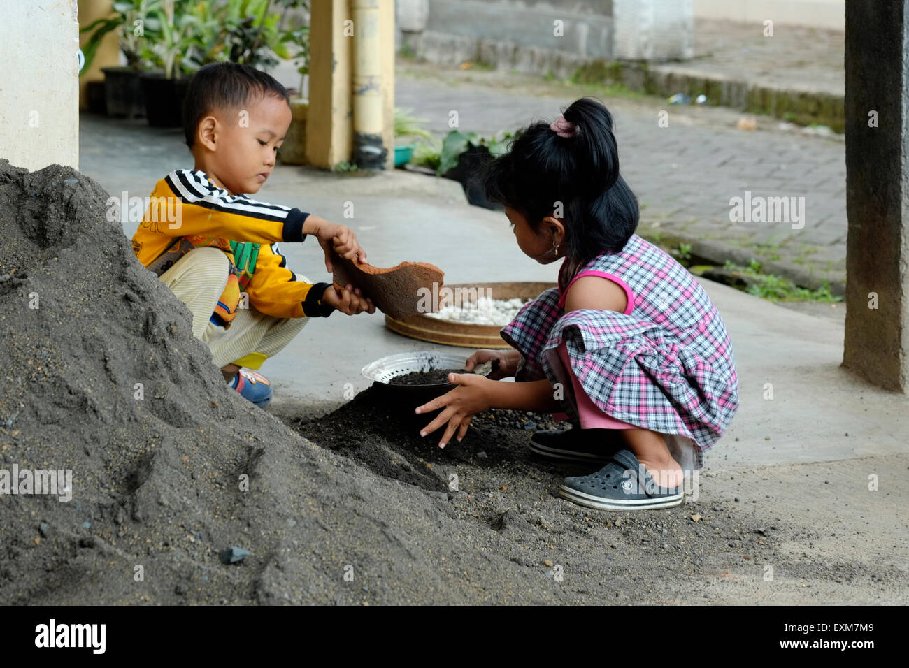 Bambini che giocano in una pila di sabbia nera essendo utilizzato per costruire una casa di estensione in un villaggio in java indonesia Foto Stock