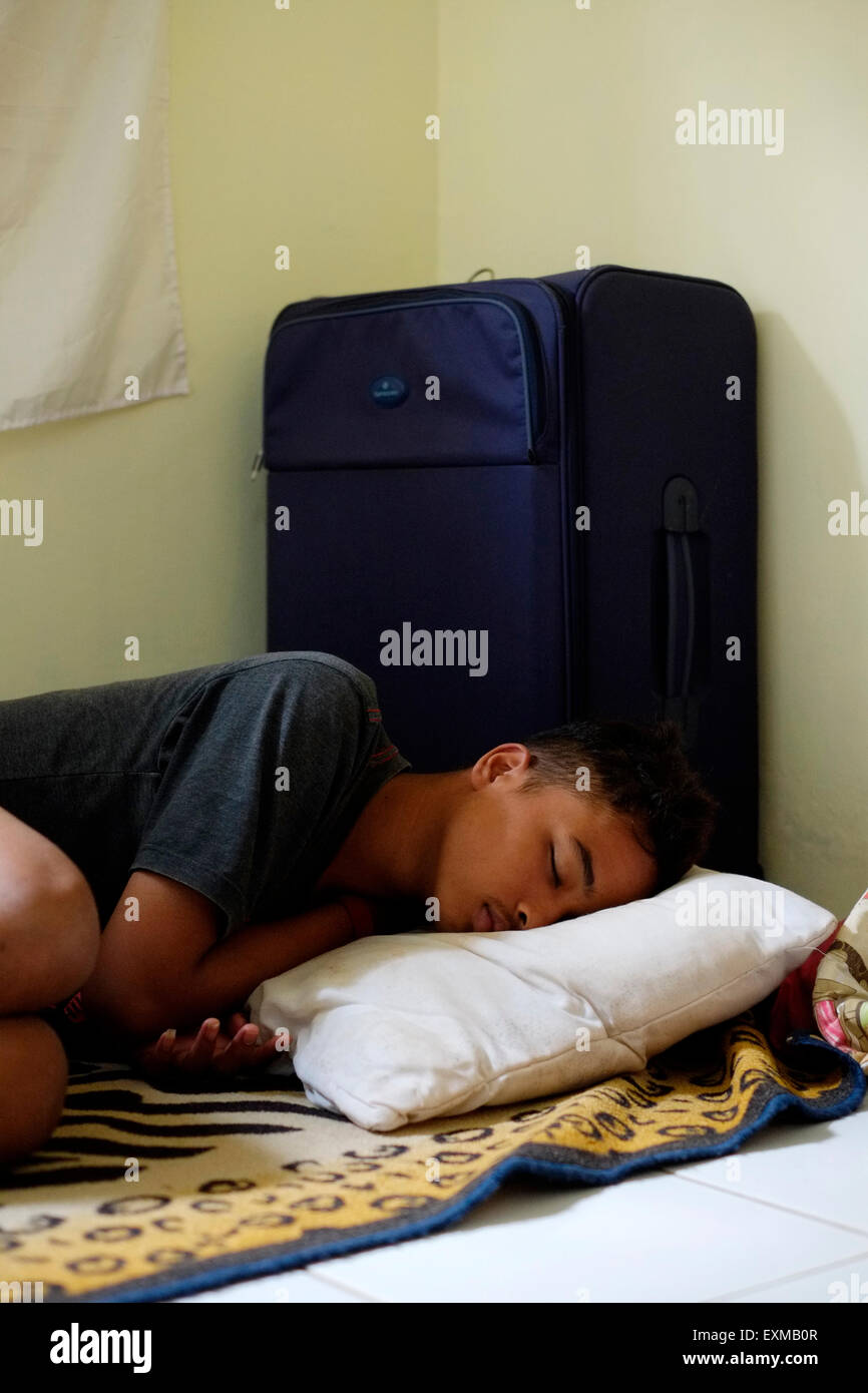 Adolescente indonesiano addormentato nella sua stanza accanto alla sua valigia dopo aver viaggiato su un lungo viaggio Foto Stock