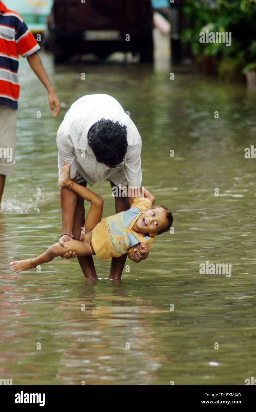Alluvioni piovose di monsoni, padre che gioca con il figlio su strada allagata, Bombay, Mumbai, Maharashtra, India, Asia Foto Stock