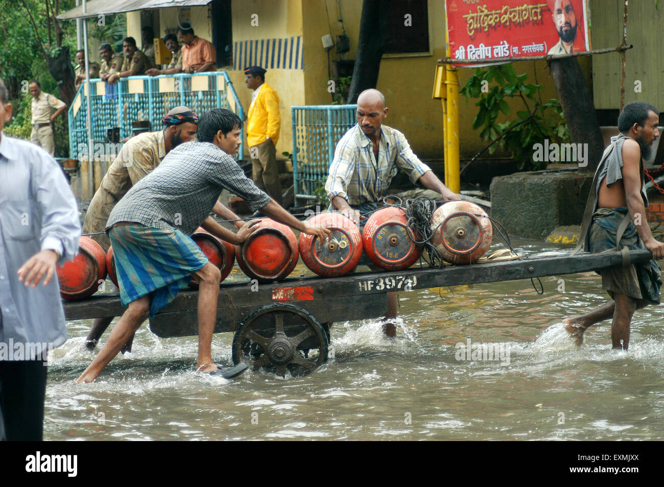 Lavoratori portano il GPL bombole di gas dal lato della spesa in allagato acqua causati a causa di forte pioggia a Bombay Mumbai; Maharashtra, India Foto Stock