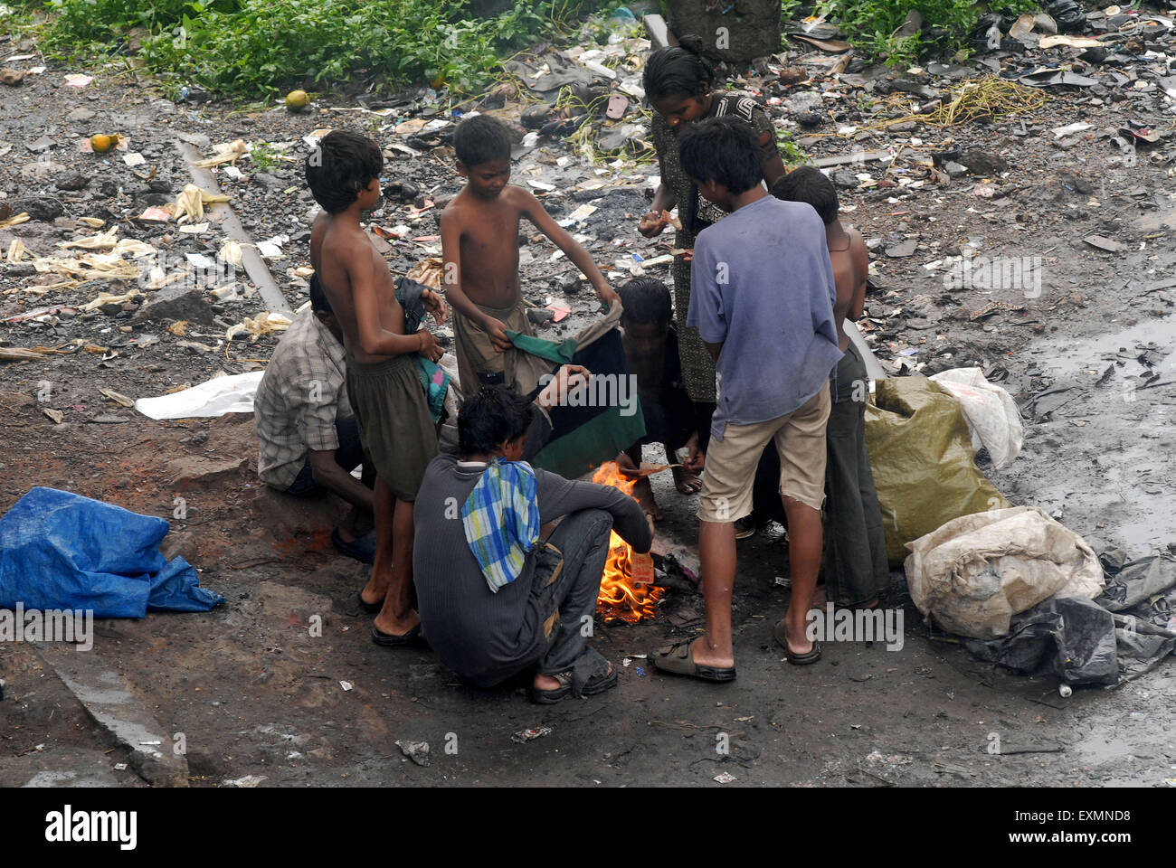 Gli abitanti degli slum di stare al fianco di binari ferroviari rendere bon fire asciugare vestiti bagnati dovuta a piogge pesanti alla stazione Kurla Mumbai Foto Stock